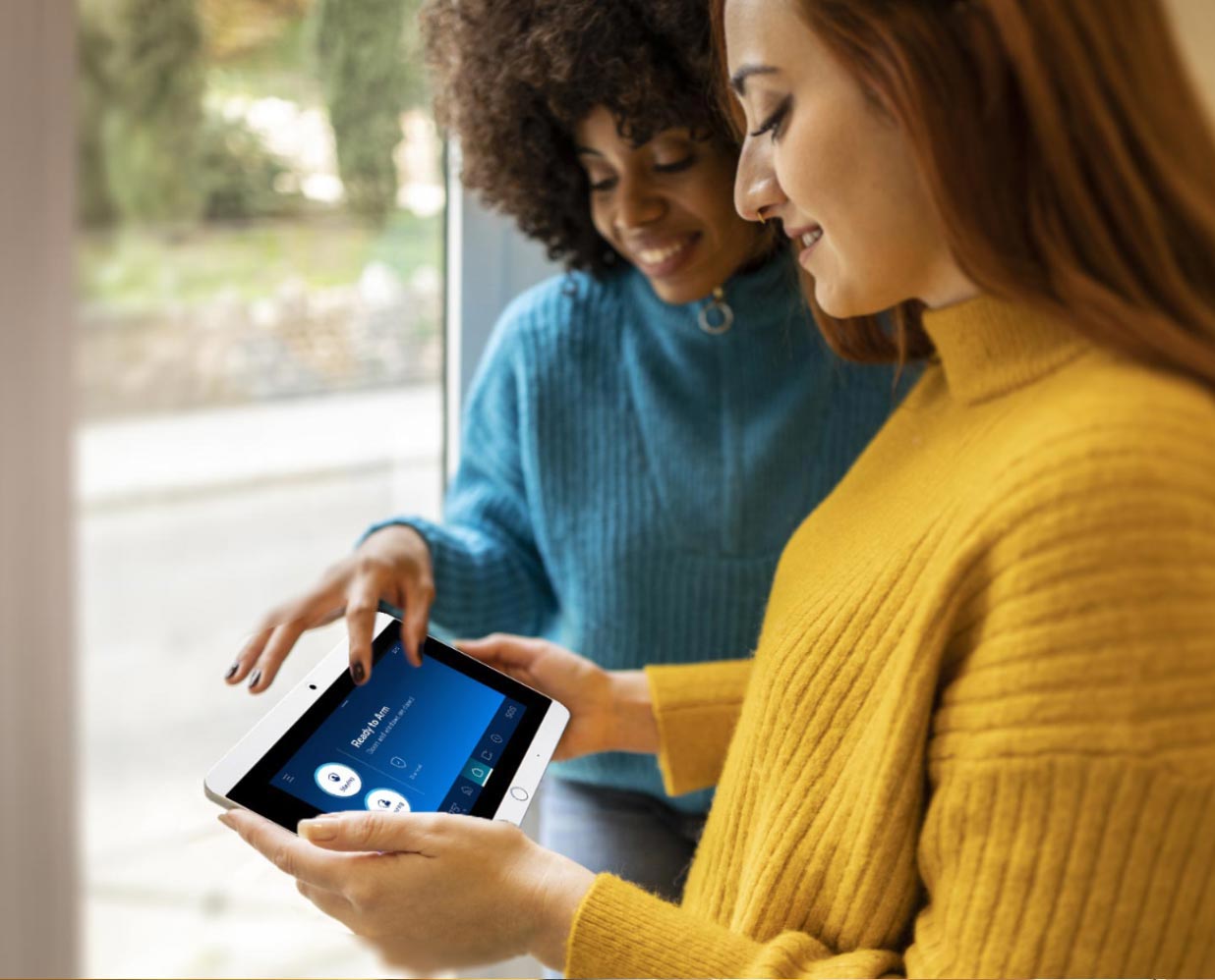 two women monitoring security with ShieldPro security panel infront of window at home